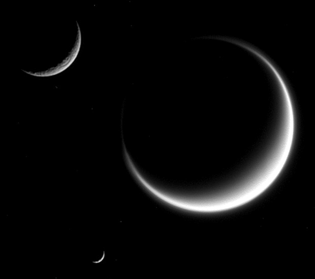 This image from NASA's Cassini spacecraft shows three moons — Rhea (top), Titan and Mimas (bottom). Titan appears fuzzy because we only see its cloud layers and light refracts within its atmosphere, extending the crescent. Image credit: NASA/JPL-Caltech/Space Science Institute.