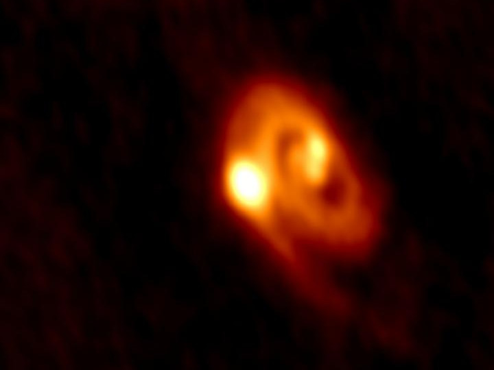 ALMA captured the image of the tri-system, the disc material around the stars and the spiral arms. The system spans a region about five times the size of our own solar system. Image credit: University of Oklahoma and ALMA.