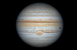 Jupiter with its orange-hued cloud bands seen through a telescope, its red spot lower centre 