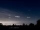 Graphic showing the close conjunction of Jupiter and Venus with other stars and contellations marked on a dark sky, above a horizon with trees in silhouette.